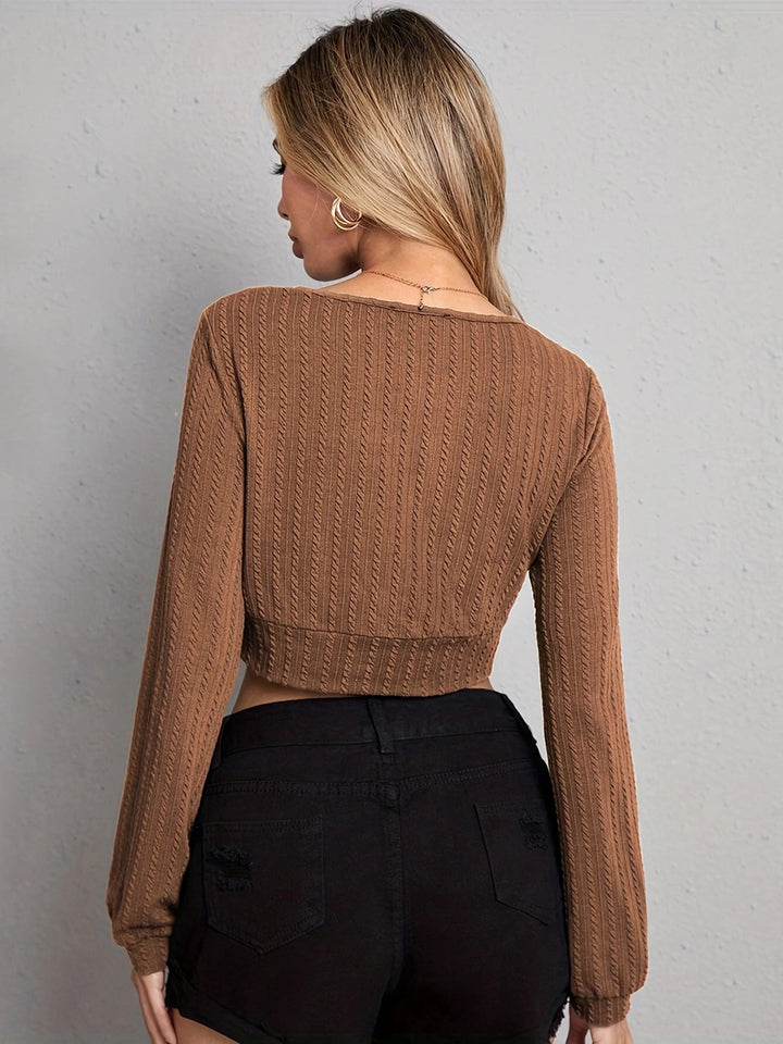Woman wearing a brown knitted sweater and black pants against a gray background