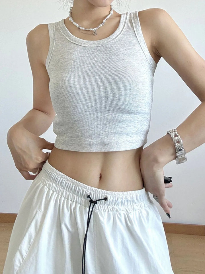 Person wearing a white sleeveless top and white pants against a plain background
