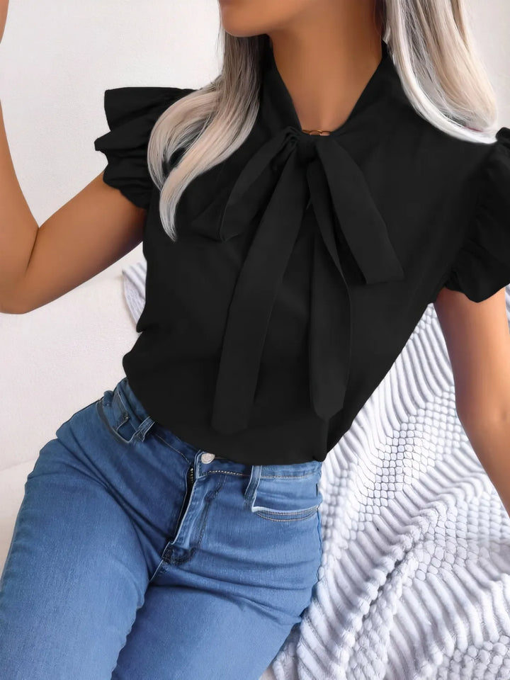 Person wearing a black blouse with a large bow and blue jeans on a white background