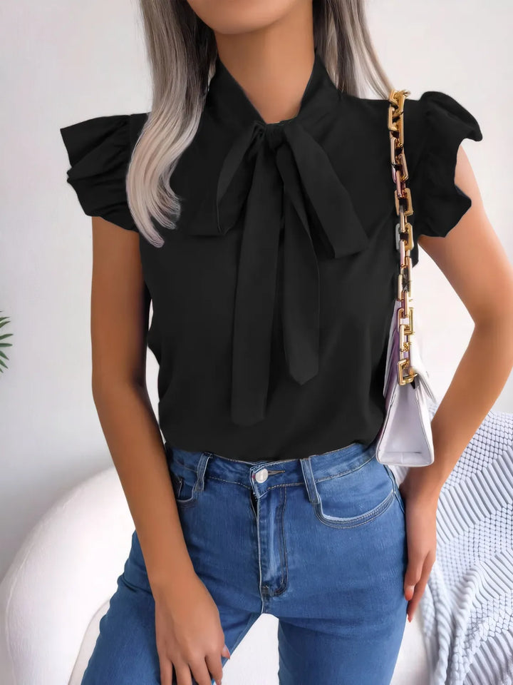 Person wearing a black blouse with a bow tie and blue jeans, holding a white handbag.
