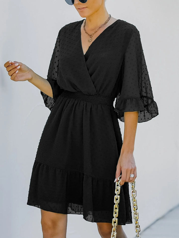 Woman wearing a black dress with sheer sleeves against a plain background