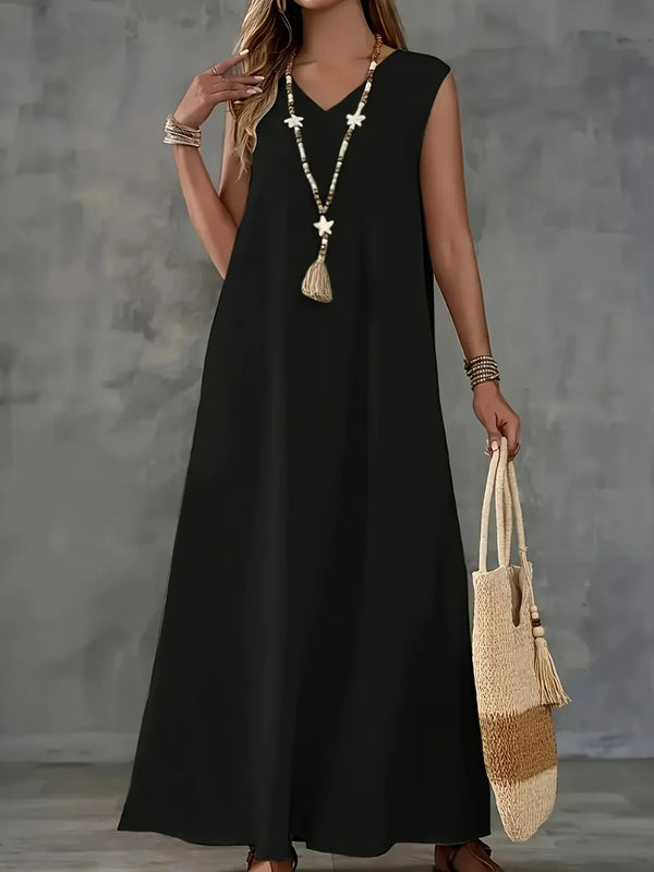 Woman wearing a black v neck maxi tank dress holding a woven bag against a gray background