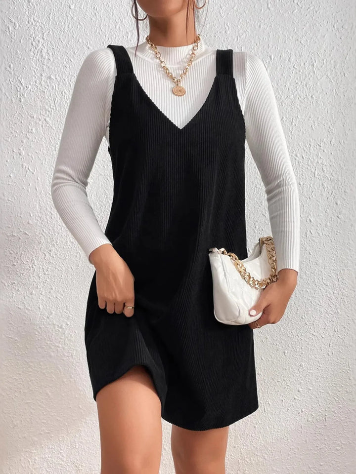 Person wearing a black casual dress over a white long-sleeve shirt, holding a white handbag against a light background