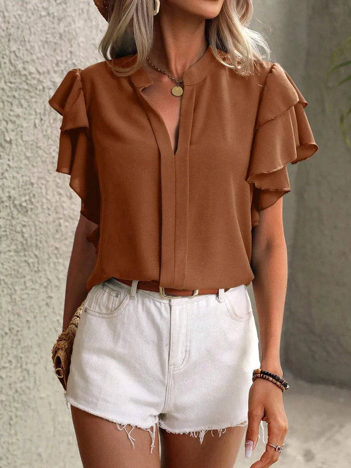 Woman wearing a brown blouse with ruffled sleeves and white shorts against a neutral background