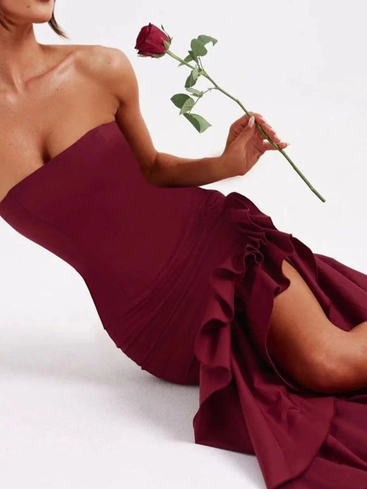 Woman in a burgundy strapless dress holding a red rose on a white background