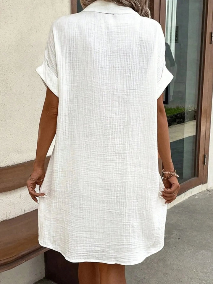 model wearing a white casual button down dress standing outside.