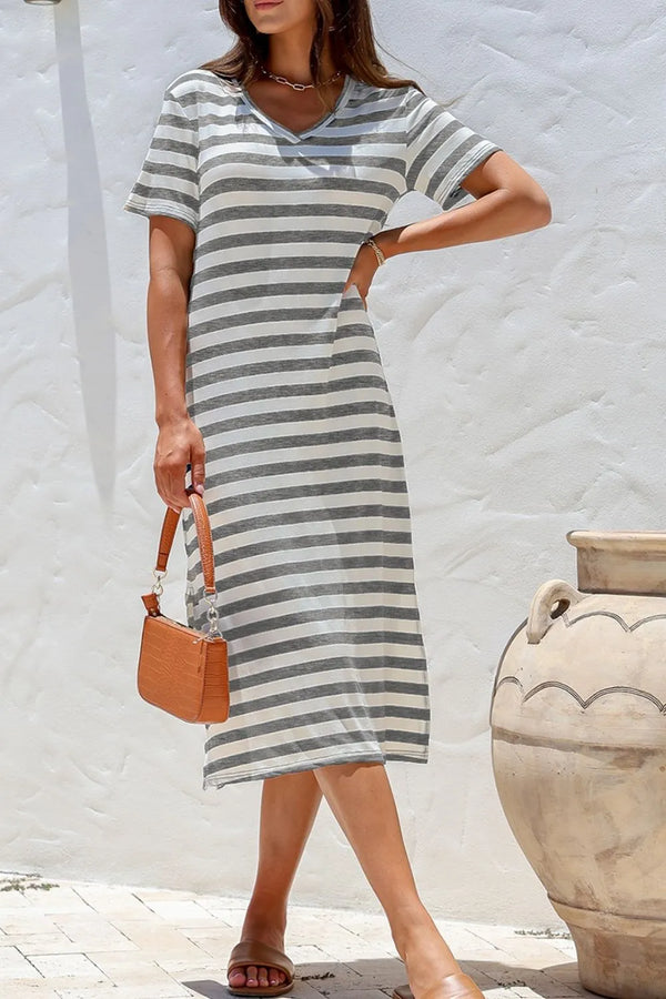 Woman wearing a casual striped dress holding a brown bag against a white wall.