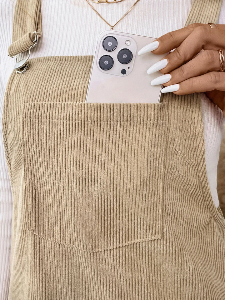 Person holding a phone in a pocket of khaki corduroy overalls.
