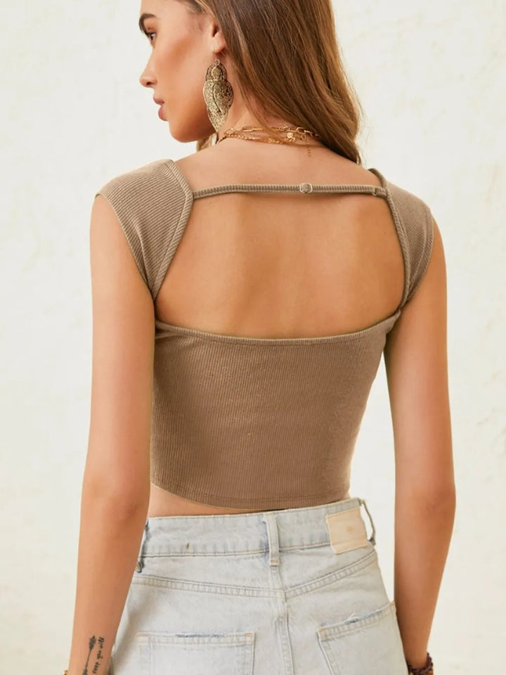 Woman wearing a brown crop top with thin straps and light blue jeans on a plain background
