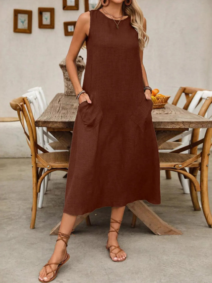 Woman wearing a dark brown midi dress standing in a room with wooden furniture.