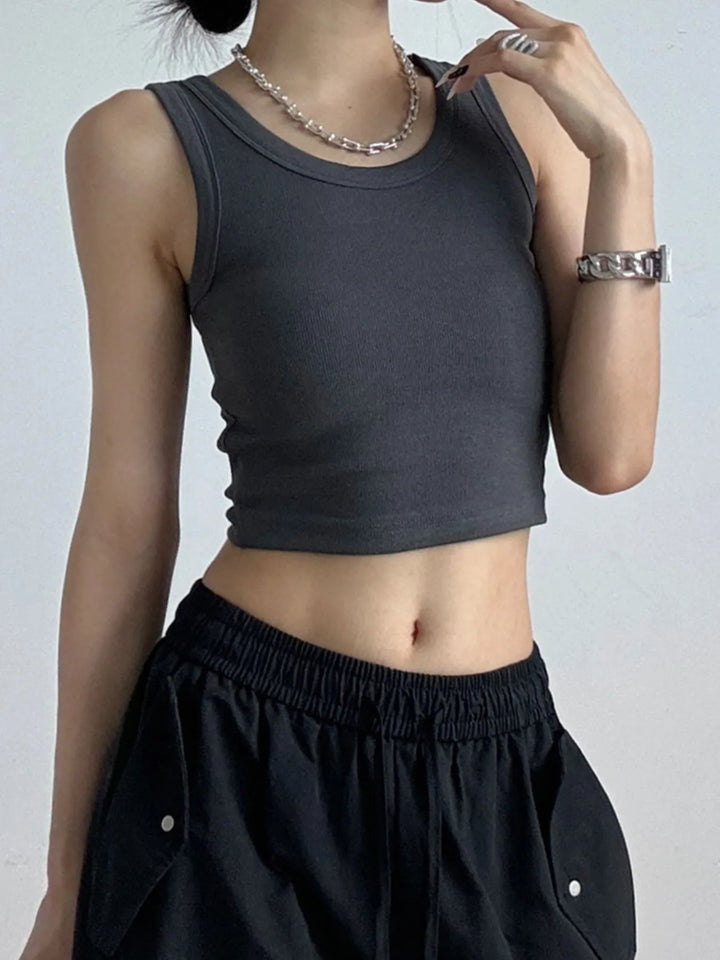 Person wearing a dark gray cropped tank top and black pants on a plain background