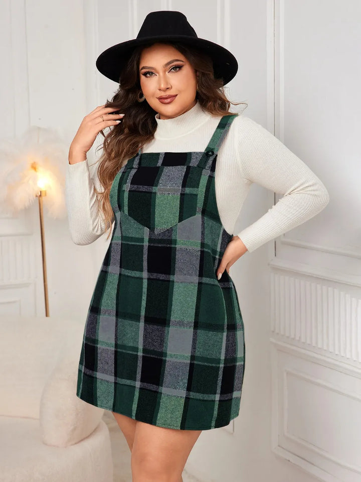 Woman wearing a green plaid dress over a white turtleneck with a black hat indoors.