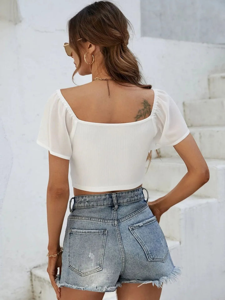 Woman wearing a white crop top and denim shorts against a light background