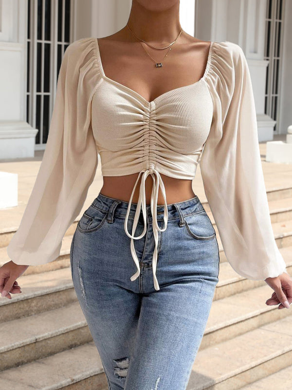 Woman wearing a beige ruched top and blue jeans outdoors.