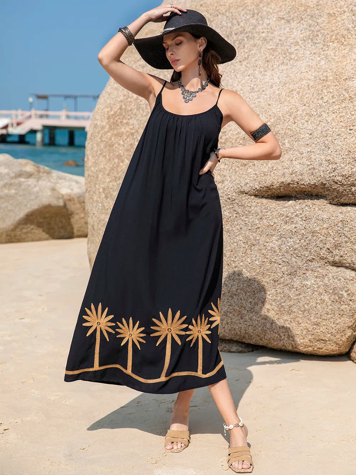Woman in a black dress with gold embroidery standing on a rocky beach.