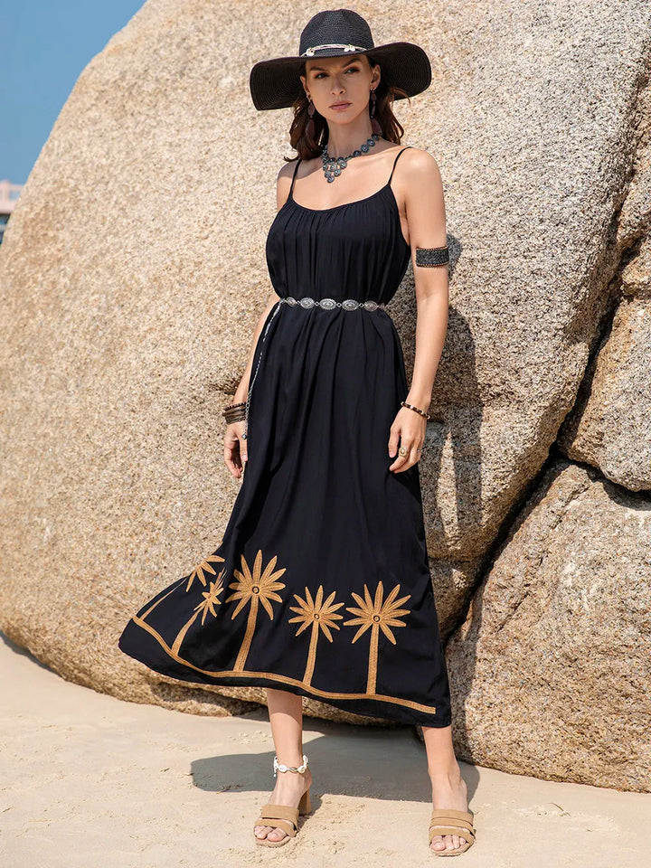 Woman in a black dress with gold palm tree patterns standing against a rocky background.