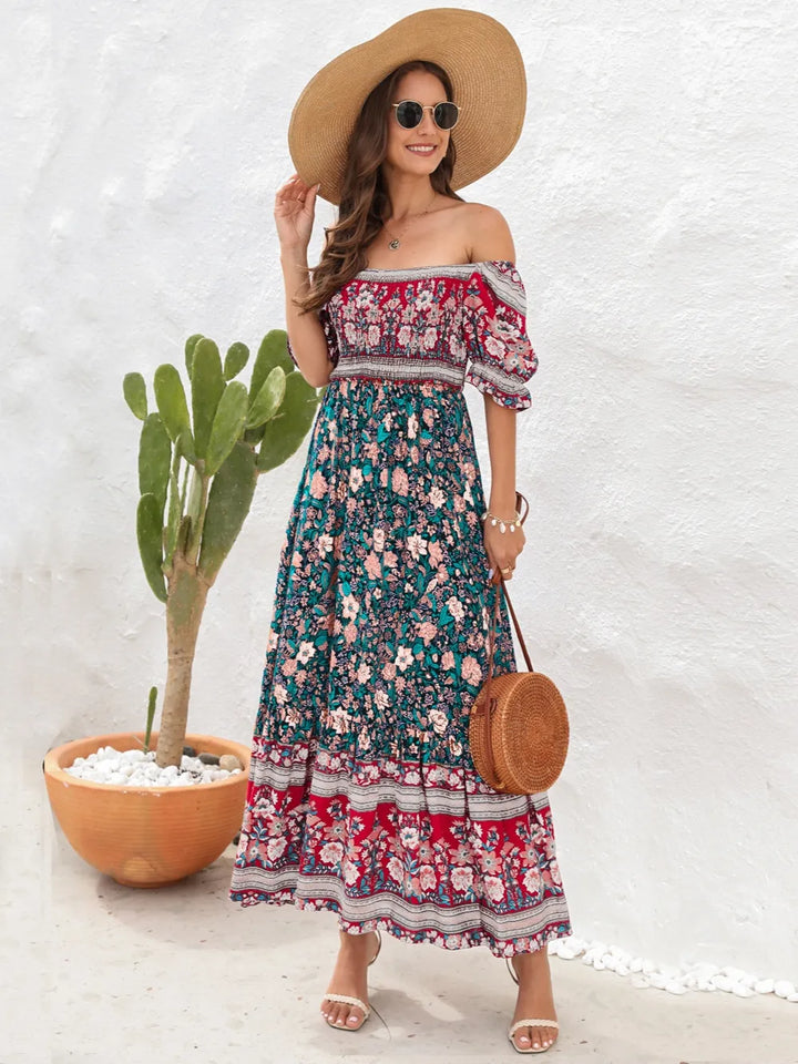 Woman in a floral midi dress with a wide-brimmed hat standing next to a cactus plant.