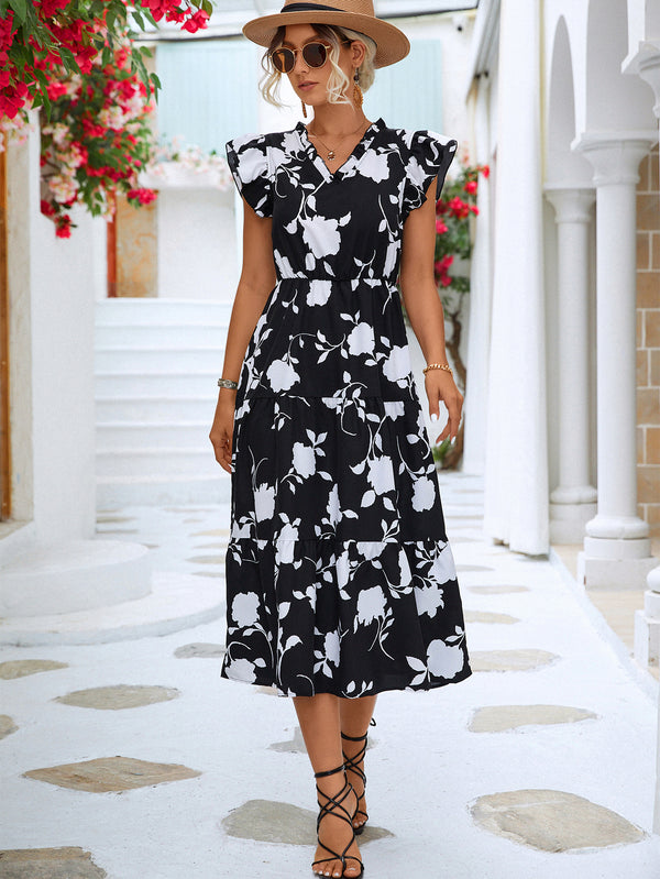 Woman wearing a black floral dress in an outdoor setting with white columns and red flowers.