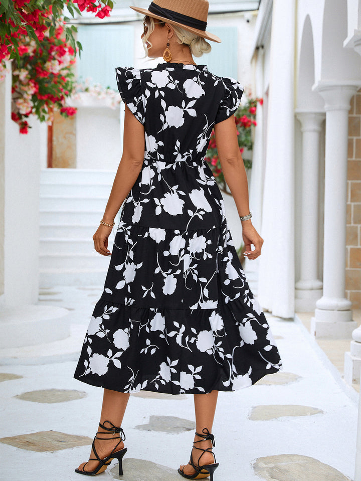Woman wearing a black floral dress in an outdoor setting with columns and flowers.