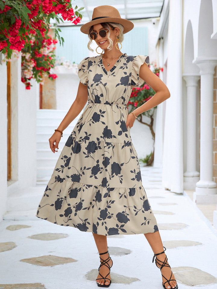 Woman in a floral dress standing in a sunlit outdoor setting with flowers and columns.