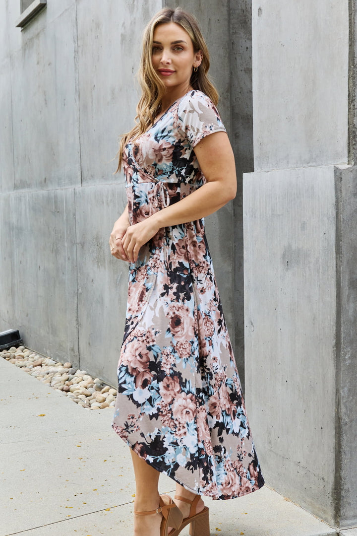 Woman wearing a floral dress standing against a concrete wall.