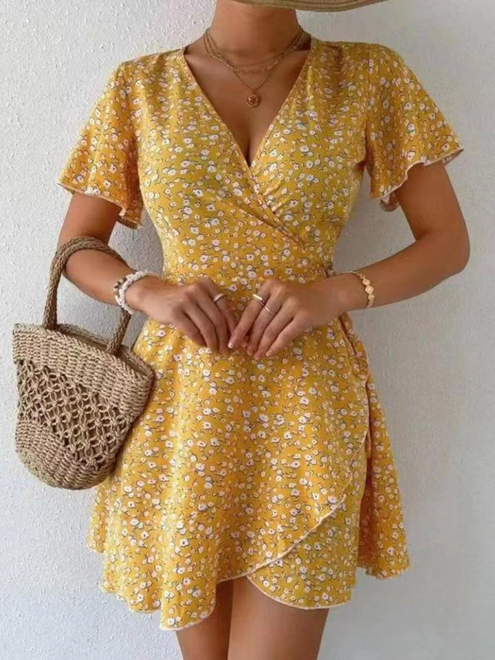Woman wearing a yellow floral dress holding a woven bag against a white background