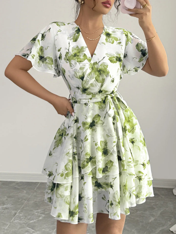 Woman wearing a white Mini Wrap dress with green floral pattern in a room.