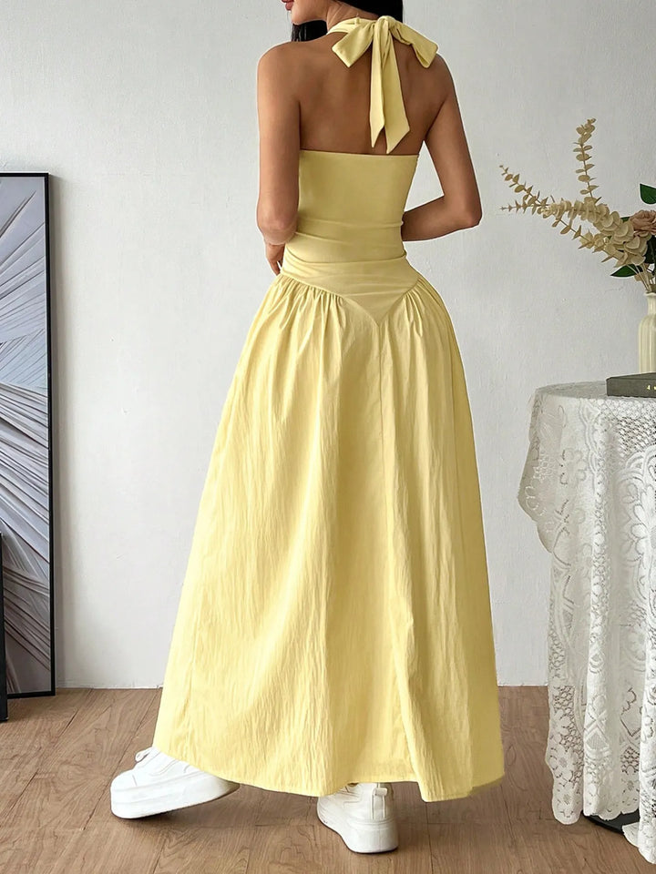 Woman wearing a yellow dress with a halter neck and tied sleeves in a room.