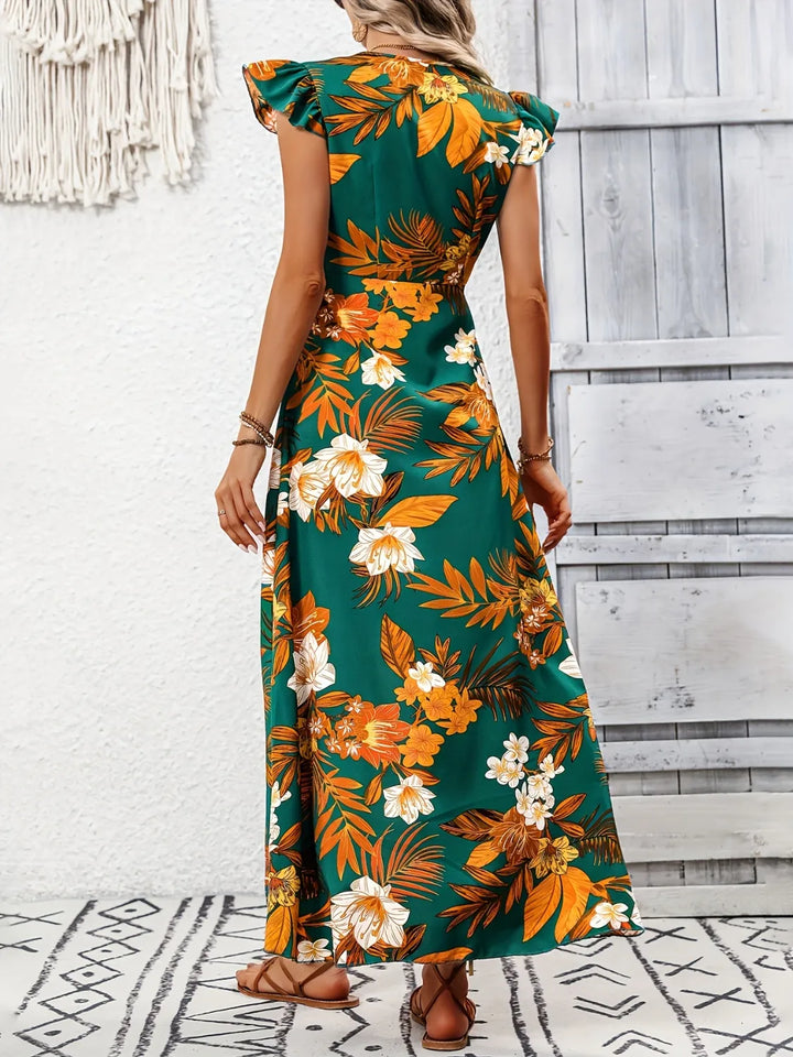 Woman wearing a floral maxi dress with orange and green pattern against a white wall.