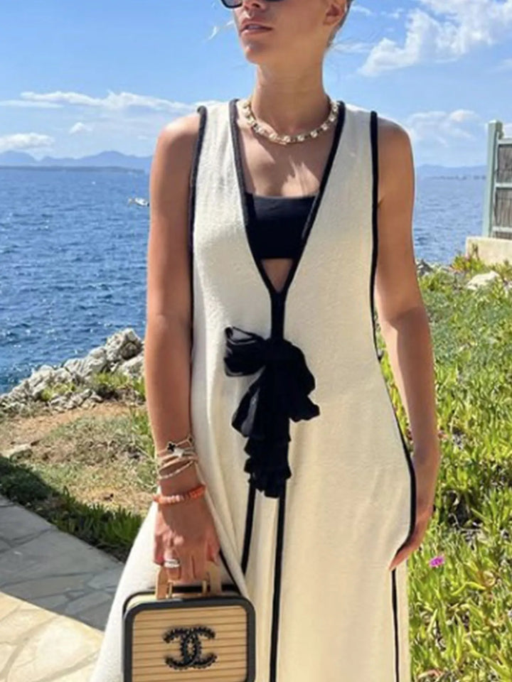 Woman in ivory maxi dress holding a Chanel handbag by the sea.