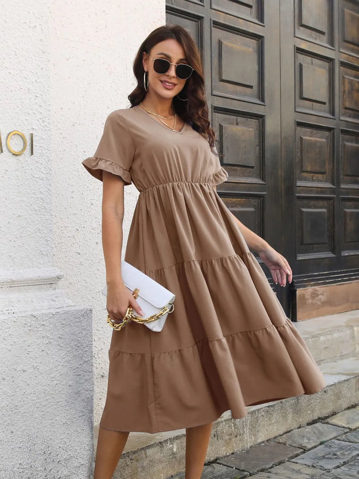 Woman in a khaki midi dress standing in front of a building entrance.