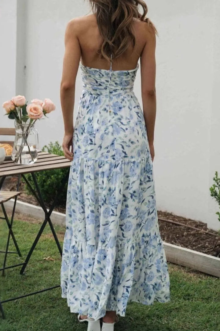 Woman wearing a floral Maxi dress standing outdoors near a table with flowers.