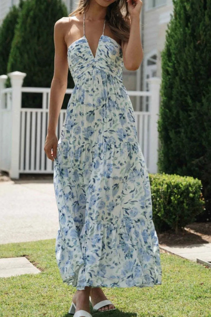 Woman wearing a floral maxi dress standing on grass with a white fence and greenery in the background