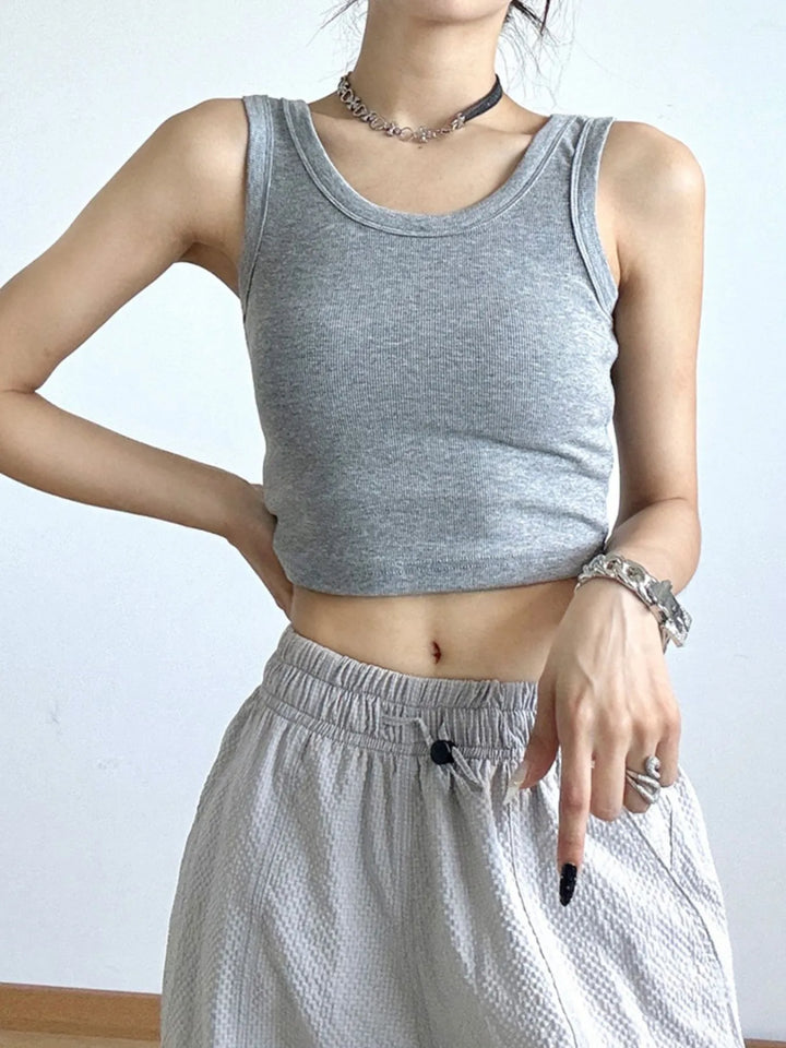 Person wearing a gray tank cropped top and light-colored pants against a plain background