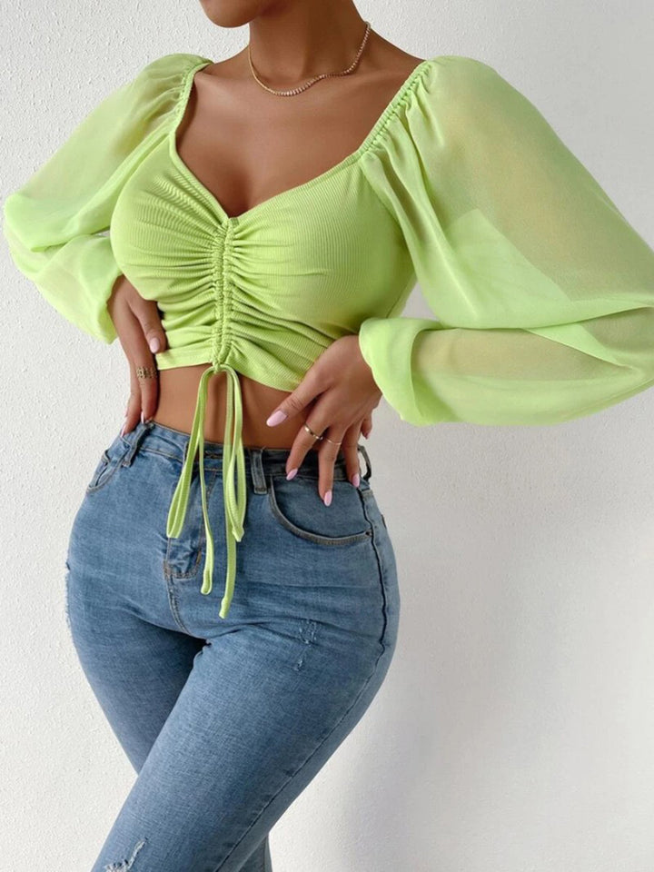 Person wearing a bright green top with sheer sleeves and blue jeans on a white background