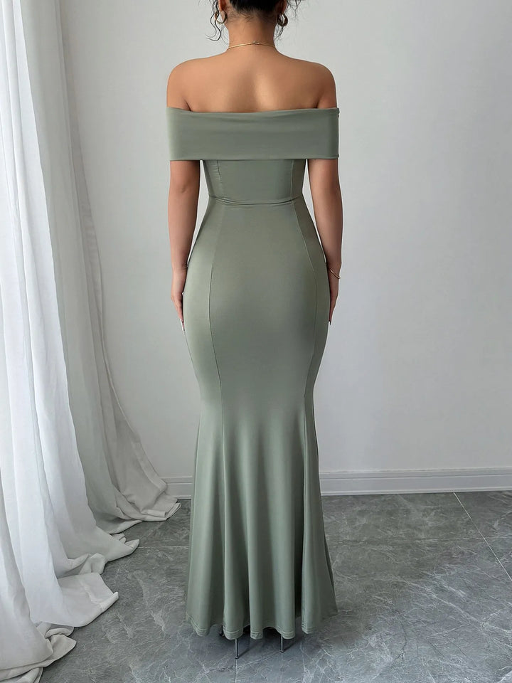 Woman wearing a sage off-shoulder gown standing against a white wall.