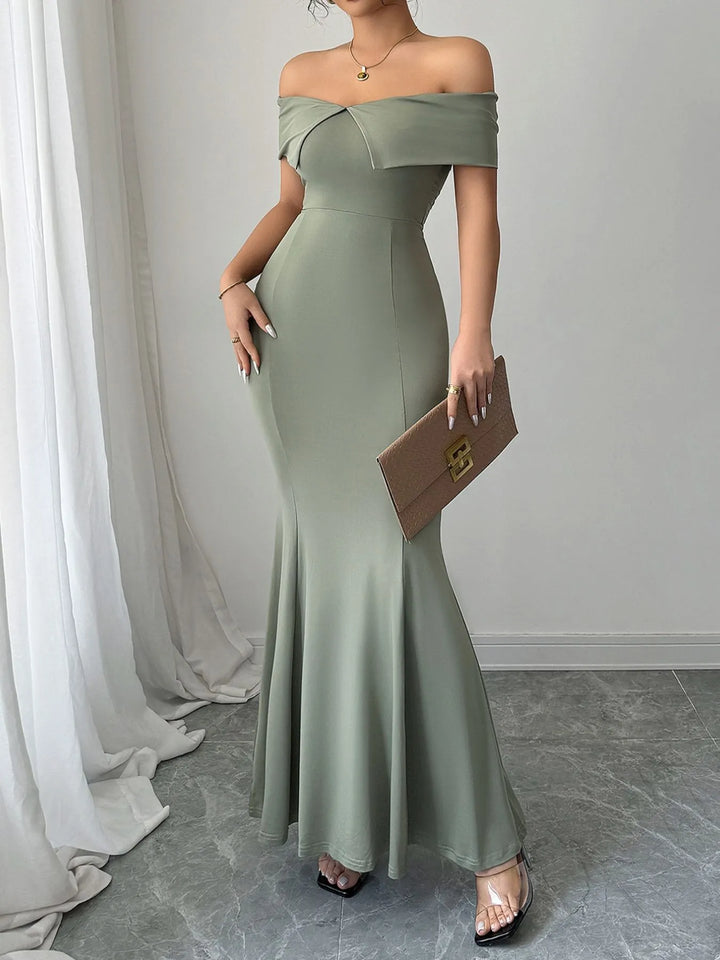 Woman wearing a sage off-shoulder gown holding a brown clutch against a neutral background