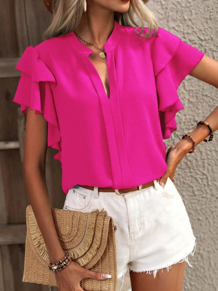 Woman wearing a bright pink blouse with ruffled sleeves, white shorts, and holding a beige clutch.