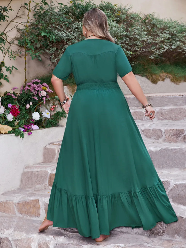 Woman in a teal maxi dress standing on stone steps with flowers and plants in the background