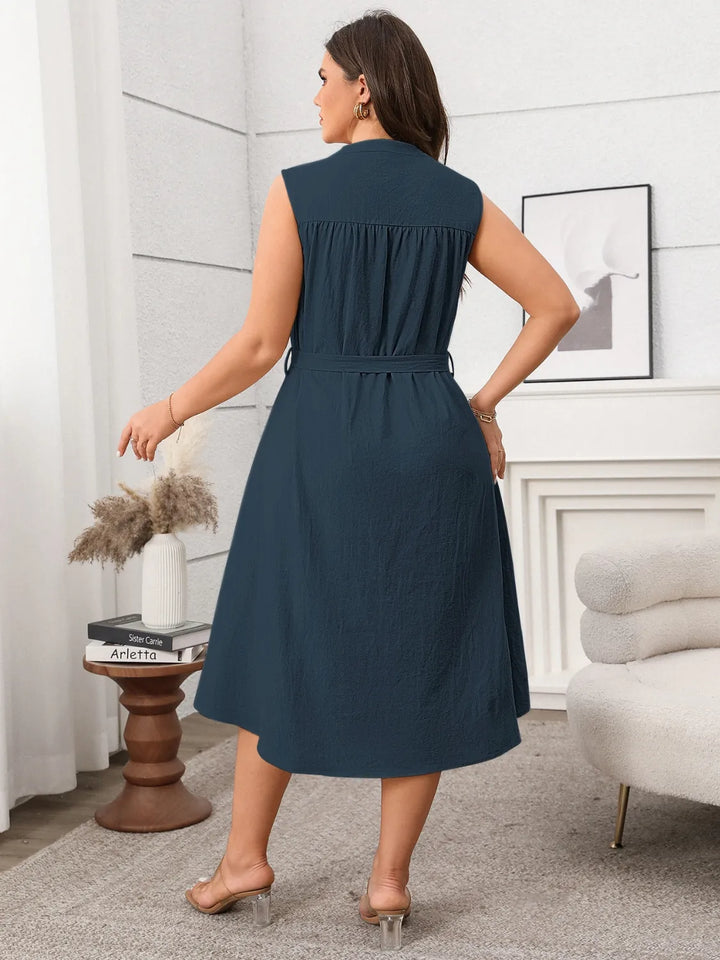 Woman wearing a navy blue midi dress in a room with a white wall and decorative items.