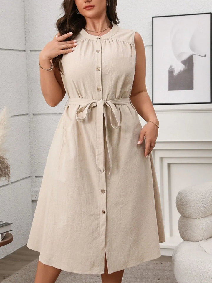 Woman wearing a tan sleeveless midi dress with buttons in a room setting.