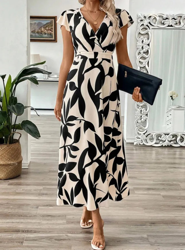 Woman wearing a black and white patterned dress holding a clutch in a room with decor elements.