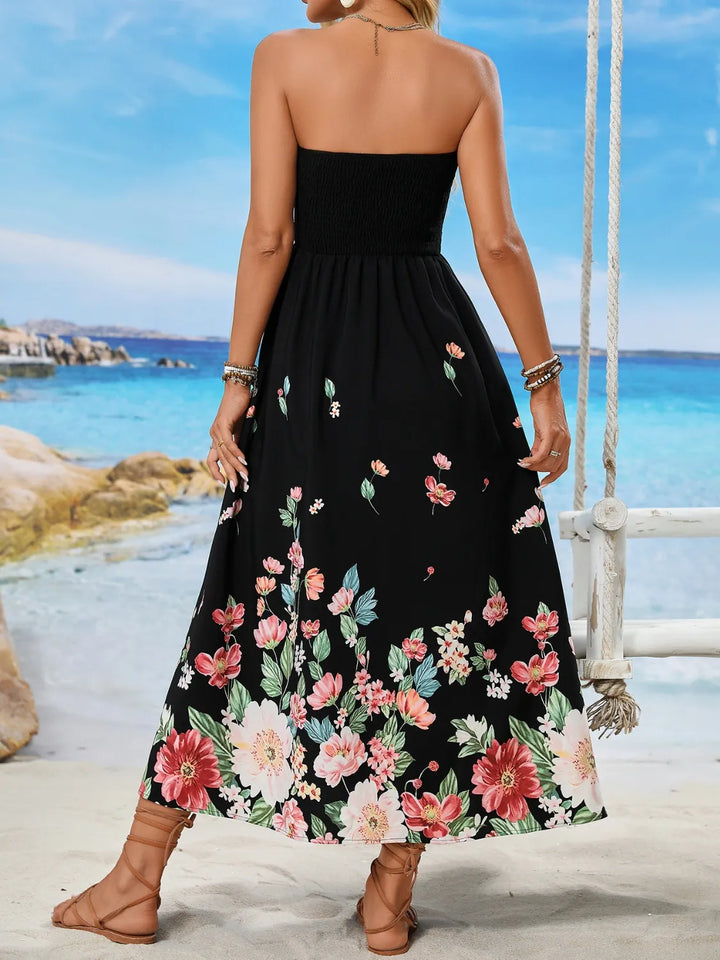 Woman wearing a black strapless dress with floral patterns on a beach.
