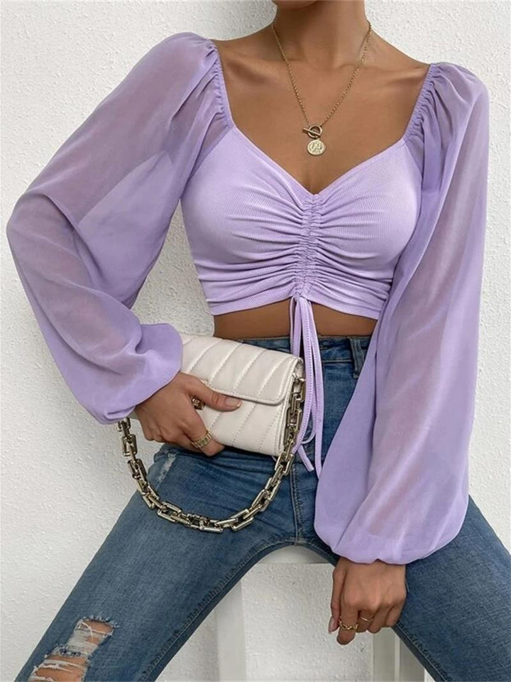Person wearing a light purple blouse with long sleeves and blue jeans, holding a white clutch.