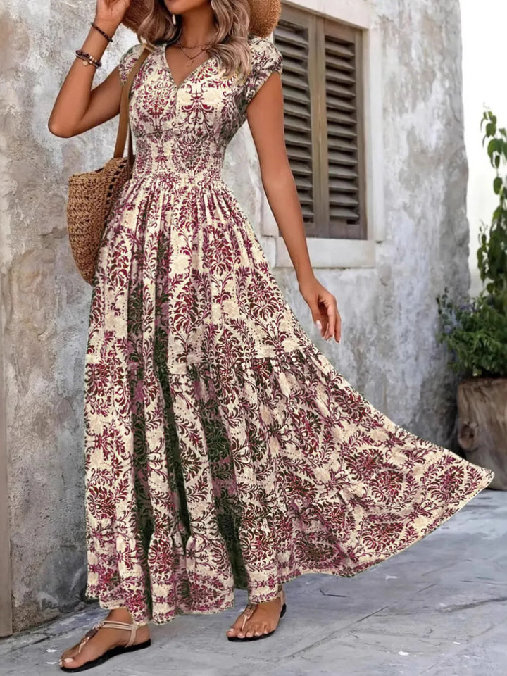 Woman wearing a purple floral maxi dress standing against a stone wall.