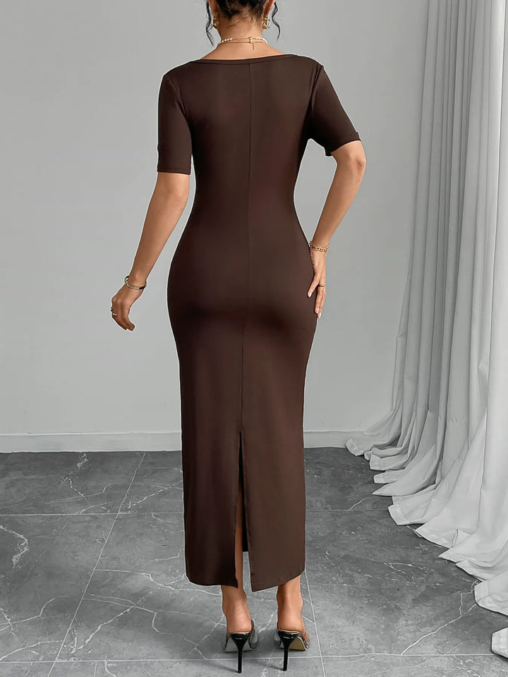 Woman wearing a chocolate midi dress with a slit, standing against a gray wall with white curtains.