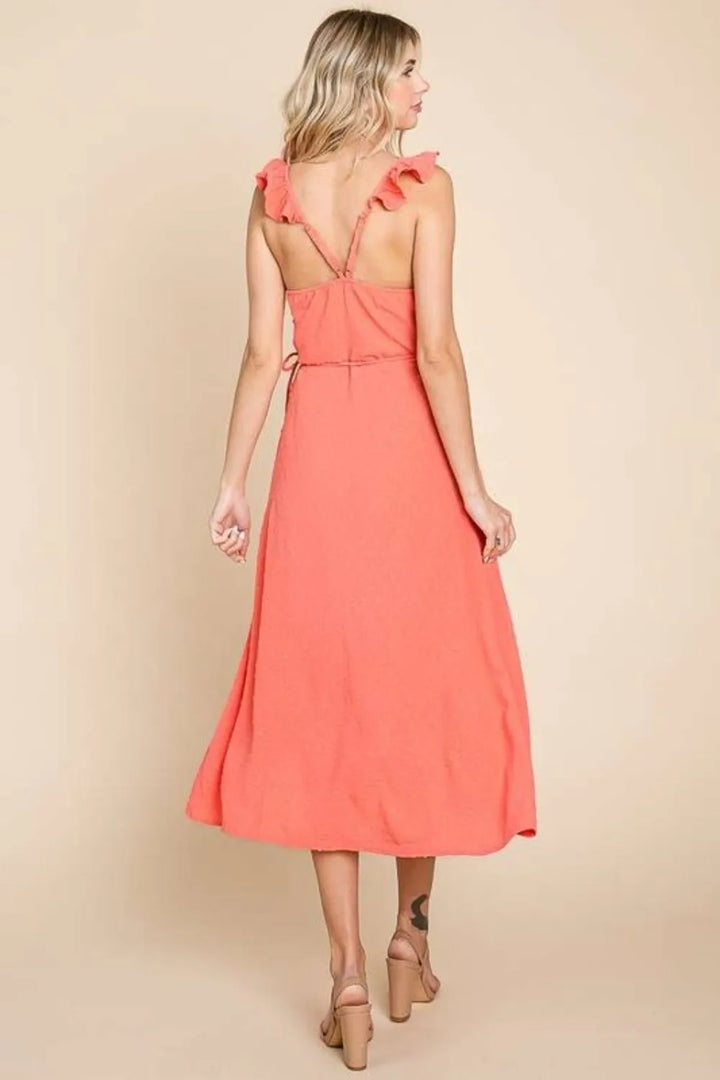 Woman wearing a coral dress with ruffled straps on a beige background