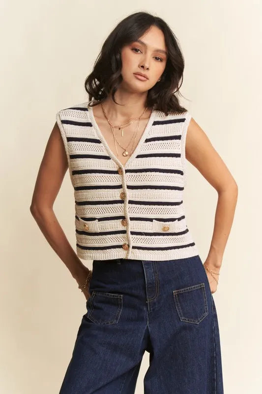Woman wearing a sleeveless striped sweater vest and blue jeans against a beige background