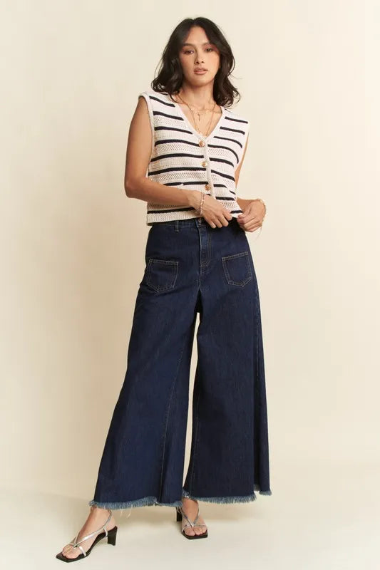 Woman wearing a striped sleeveless top and wide-leg jeans against a beige background