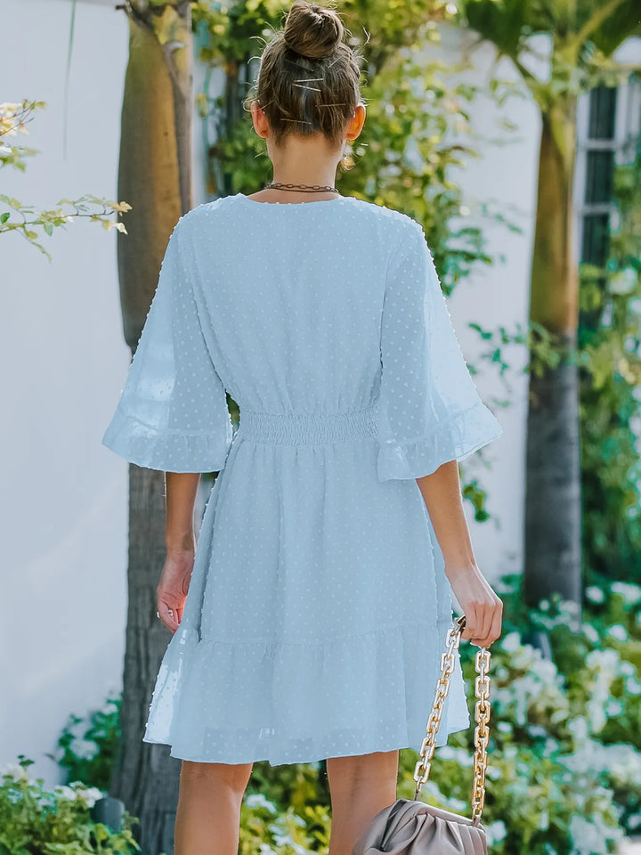 Woman in a light blue dress standing outdoors with greenery in the background